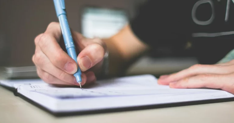 Personne qui écrit la liste des verbes irréguliers anglais dans un cahier
